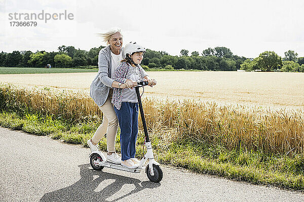 Glückliche Enkelin und Großmutter spielen beim Fahren mit dem Roller an einem sonnigen Tag