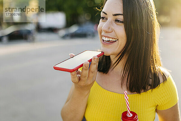 Glückliche junge Frau  die auf der Straße mit einem Mobiltelefon spricht