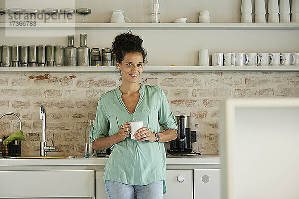 Lächelnde Geschäftsfrau  die eine Kaffeetasse hält  während sie in einer Cafeteria steht