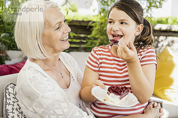 Enkelin isst Kuchen  während sie mit ihrer Großmutter auf dem Balkon sitzt