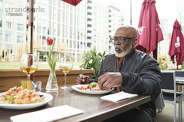 Älterer Mann isst Essen in einem Straßencafé