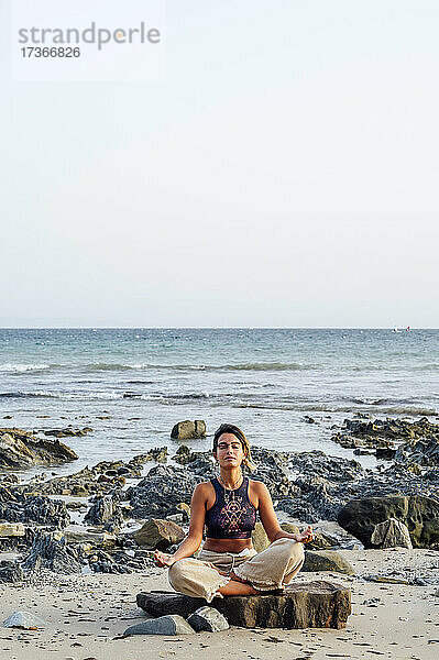 Frau im Lotussitz auf einem Felsen am Strand