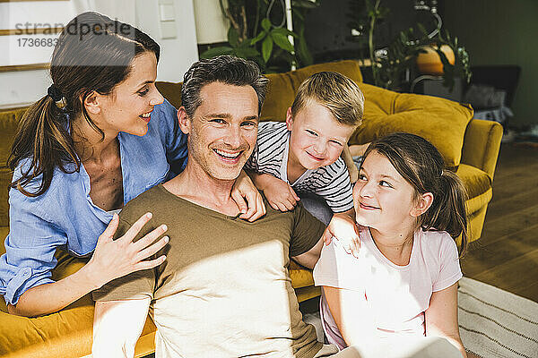 Frau schaut auf lächelnden Mann  der mit Kindern in der Nähe des Sofas zu Hause sitzt