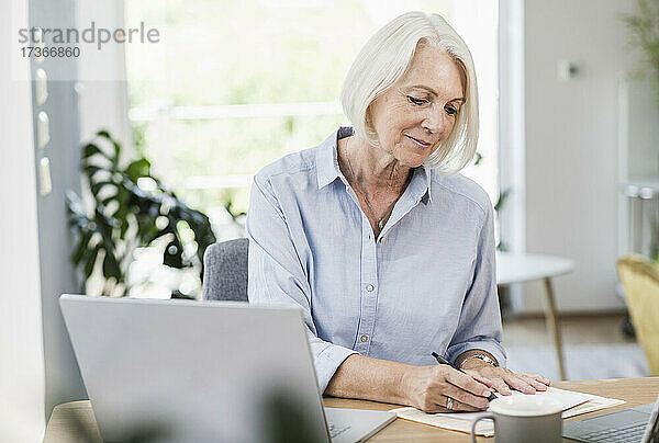 Weibliche Fachkraft beim Schreiben auf Papier im Home Office