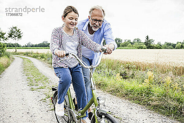 Großvater bringt seiner Enkelin auf einem unbefestigten Weg das Radfahren bei