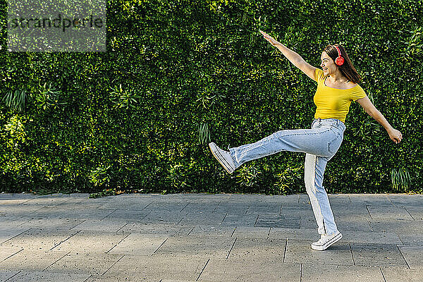 Fröhliche junge Frau  die tanzt  während sie über Kopfhörer auf dem Fußweg Musik hört