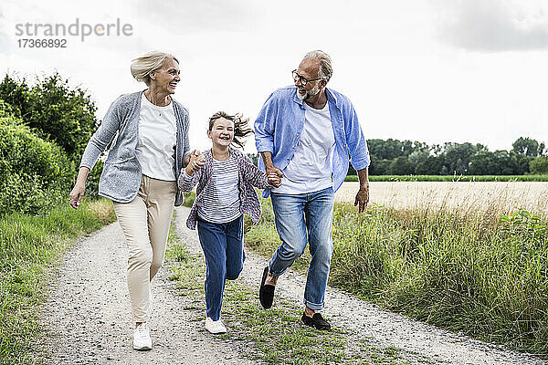 Fröhliche Großeltern spielen mit ihrer Enkelin  während sie auf einem Feldweg laufen