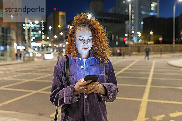 Junge Frau benutzt ihr Smartphone auf einer nächtlichen Kreuzung