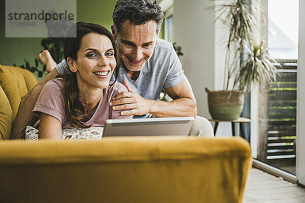 Lächelndes Paar benutzt digitales Tablet auf dem Sofa zu Hause