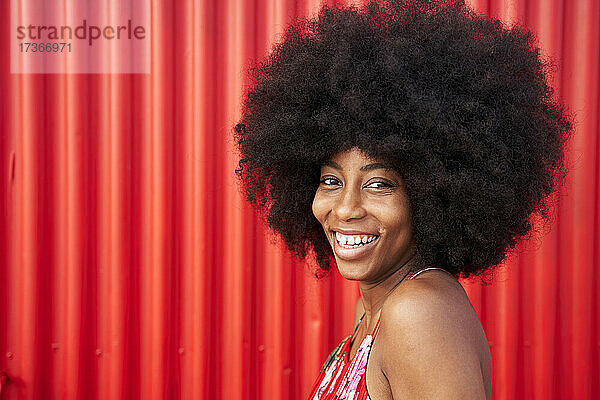 Fröhliche junge Frau lächelnd an roter Wand