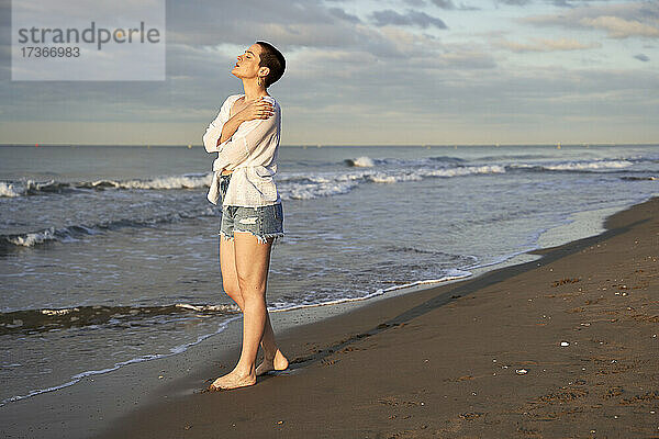 Junge Frau umarmt sich selbst  während sie am Strand steht