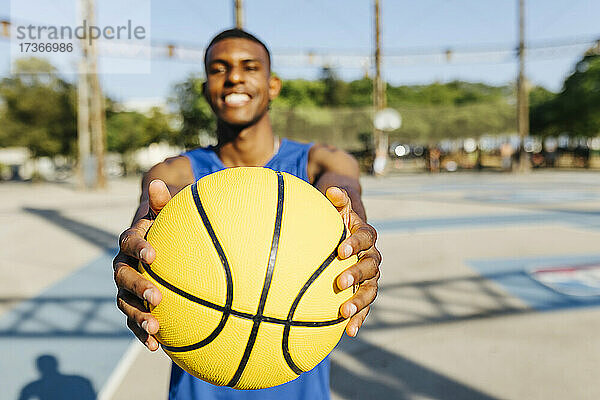 Lächelnder Mann mit gelbem Basketball auf dem Sportplatz