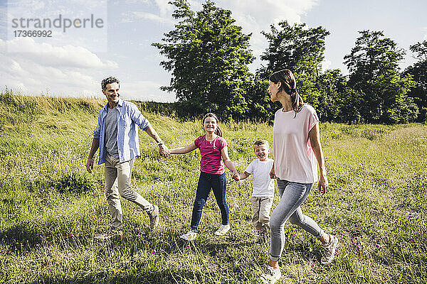 Lächelnde Familie  die sich beim Spazierengehen im Gras an den Händen hält
