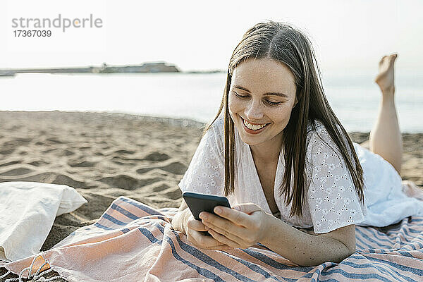Junge Frau benutzt ein Mobiltelefon  während sie auf einem Strandtuch liegt