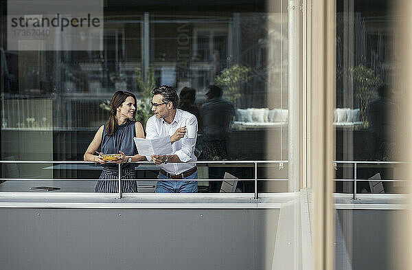 Männliche und weibliche Kollegen diskutieren auf dem Balkon eines Büros