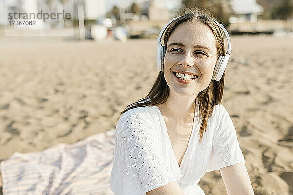 Glückliche junge Frau  die am Strand Musik über drahtlose Kopfhörer hört