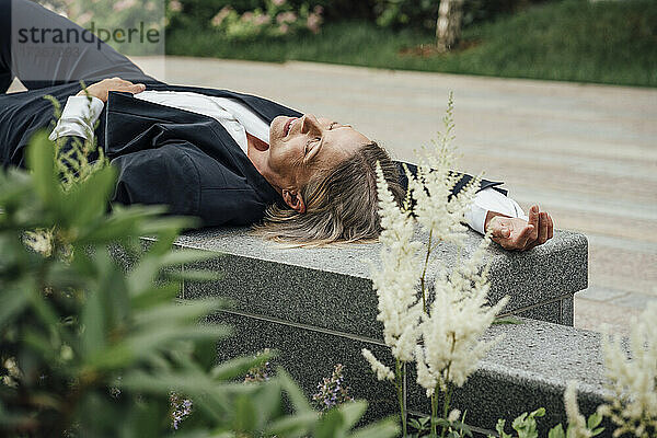 Geschäftsfrau mit geschlossenen Augen entspannt auf einer Bank im Büropark