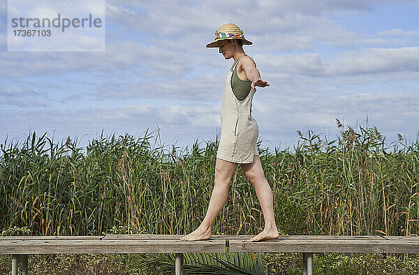 Junge Frau mit Hut balanciert auf der Strandpromenade