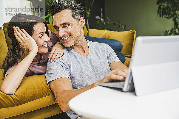 Mann und Frau schauen sich an  während sie ein digitales Tablet zu Hause benutzen