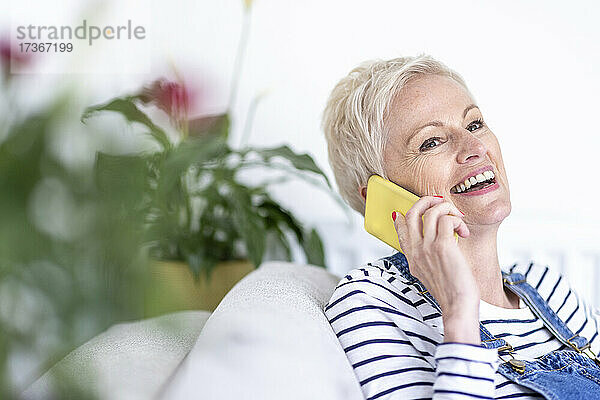 Lächelnde reife Frau  die zu Hause mit ihrem Smartphone telefoniert