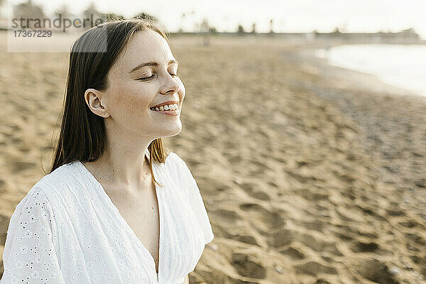 Lächelnde Frau  die mit geschlossenen Augen am Strand sitzt und träumt