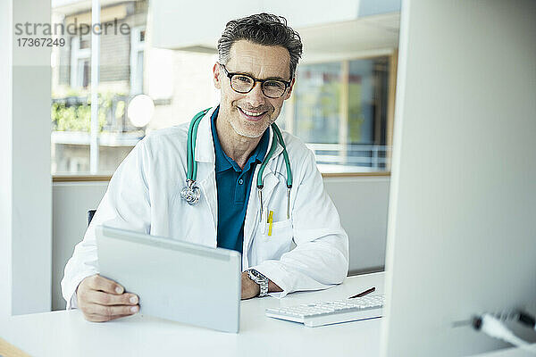 Lächelnder männlicher Arzt mit digitalem Tablet im Büro