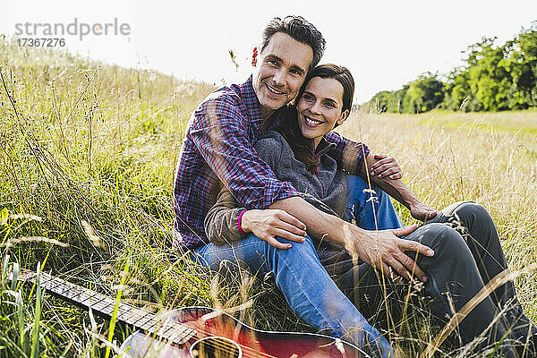 Lächelndes Paar sitzt zusammen bei der Gitarre im Gras