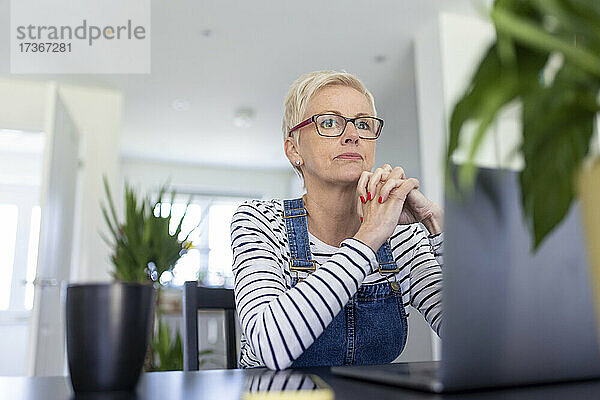 Nachdenkliche Geschäftsfrau mit gefalteten Händen  die am Schreibtisch im Heimbüro sitzt