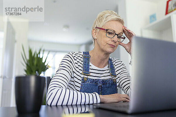 Besorgte Geschäftsfrau mit dem Kopf in der Hand  während sie im Heimbüro auf ihren Laptop schaut