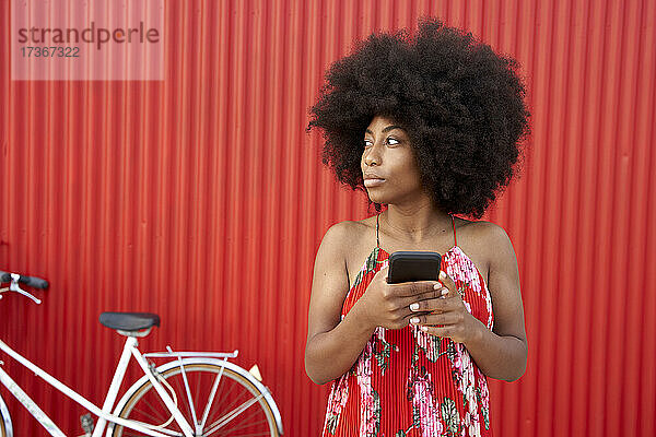 Frau hält Handy  während sie vor einer roten Wand steht