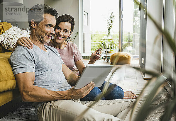Frau hält Kreditkarte  während sie mit einem Mann zusammensitzt  der ein digitales Tablet zu Hause benutzt