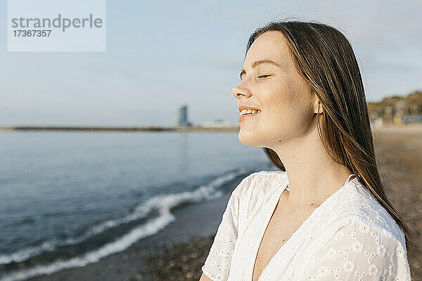 Lächelnde junge Frau mit geschlossenen Augen am Strand