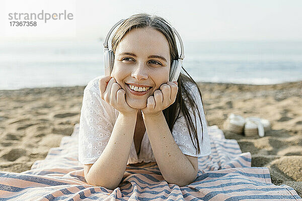 Lächelnde Frau mit Händen am Kinn hört Musik am Strand