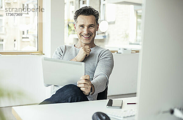 Lächelnder Geschäftsmann mit digitalem Tablet im Büro sitzend
