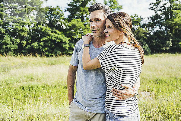 Frau  die einen Mann umarmt  während sie an einem sonnigen Tag im Gras steht