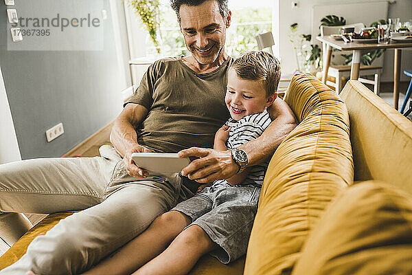 Mann sitzt mit seinem Sohn auf dem Sofa und benutzt zu Hause sein Smartphone