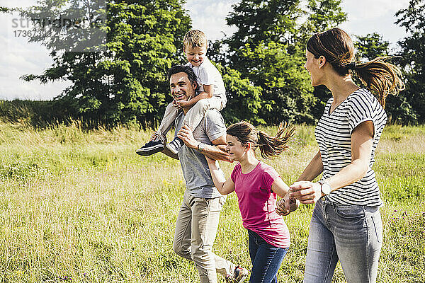 Glückliche Familie  die sich an den Händen hält  während sie an einem sonnigen Tag im Gras läuft