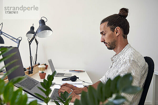 Männlicher Berufstätiger bei der Arbeit am Laptop im Büro