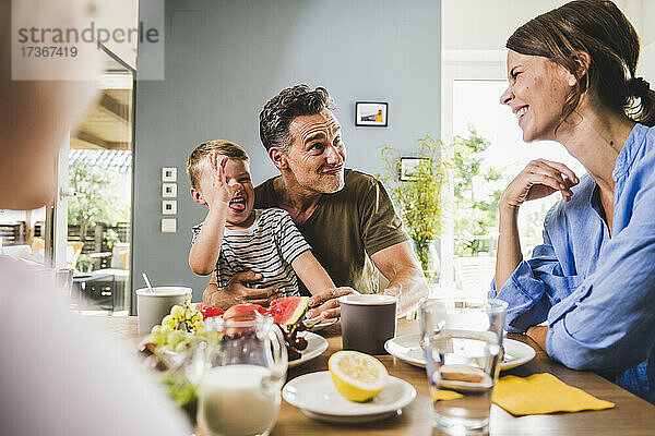 Verspielter Vater und Sohn necken Frau beim Frühstück zu Hause