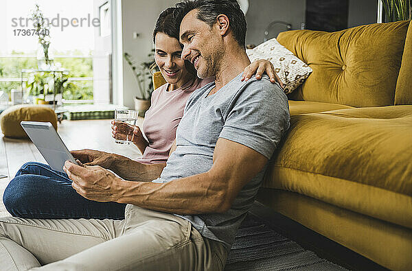 Frau hält Wasserglas  während Mann digitales Tablet zu Hause benutzt