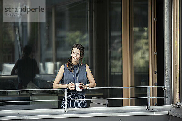 Geschäftsfrau hält Kaffeetasse  während sie auf dem Balkon des Büros steht
