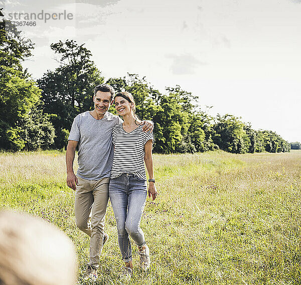 Lächelndes Paar  das an einem sonnigen Tag im Gras spazieren geht