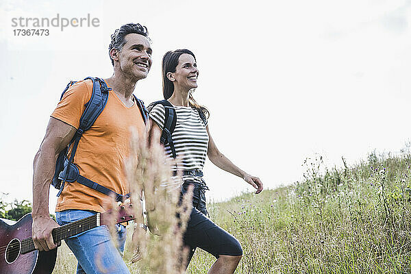 Paar mit Rucksäcken lächelnd beim Gehen auf Gras
