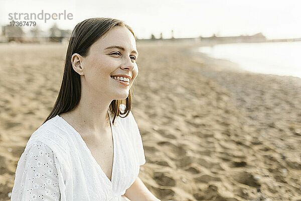 Lächelnde junge Frau am Strand sitzend