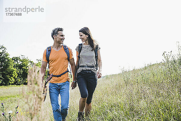Lächelndes Paar mit Rucksäcken  das sich beim Wandern im Gras unterhält