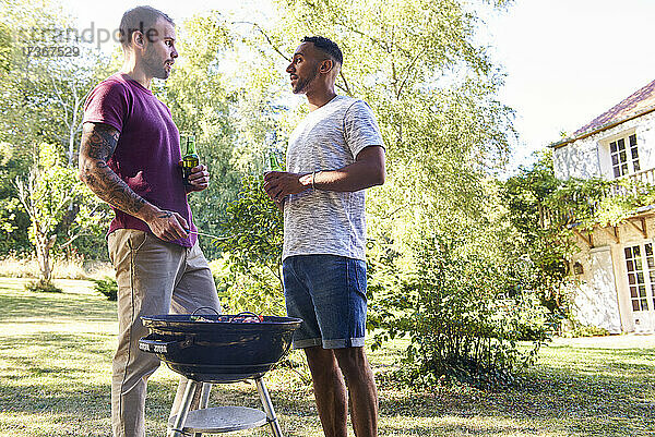 Junge Männer mit Bierflaschen stehen am Grill