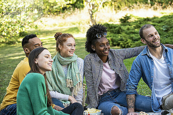 Glückliche junge Freunde sitzen zusammen in einem öffentlichen Park
