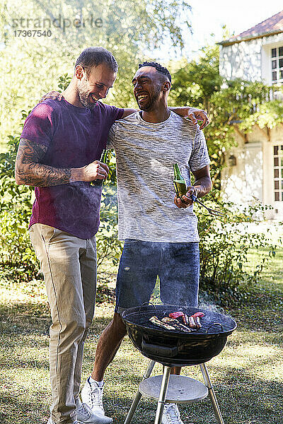 Junge Männer mit Bierflaschen stehen am Grill