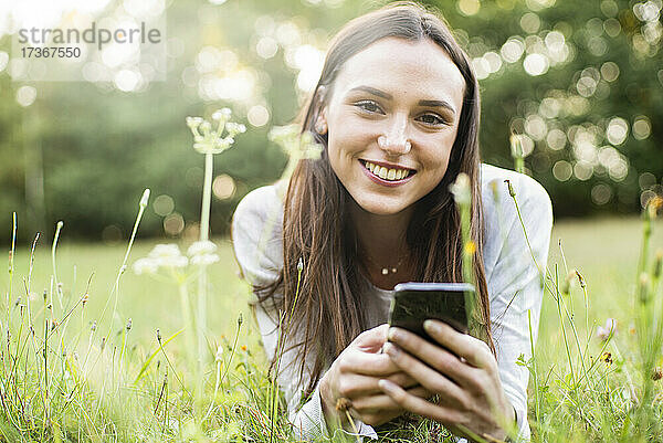Porträt einer jungen Frau  die ihr Smartphone benutzt  während sie im Park liegt
