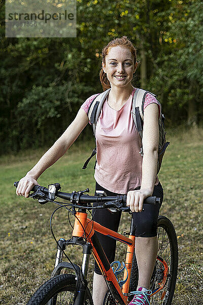 Lächelnde junge Frau sitzt auf einem Fahrrad im Wald